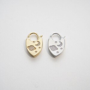 May include: Two heart-shaped lock charms with a moon, stars, and planet design. The charms are made of metal and have a silver and gold finish. The charms are adorned with small clear crystals.