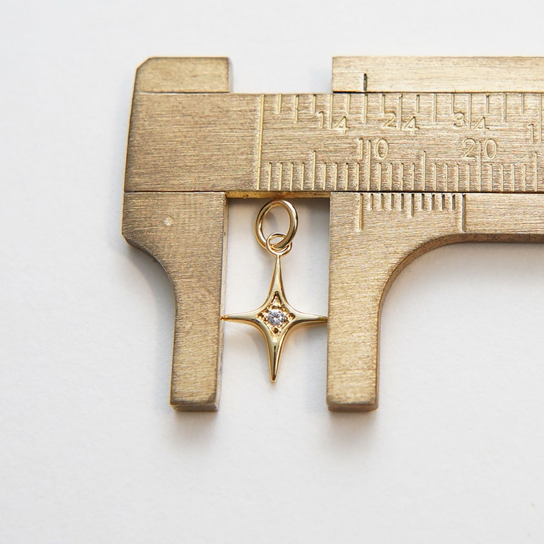 May include: A gold star charm with a clear rhinestone in the center, measured with calipers. The charm is approximately 1.5 cm in length.