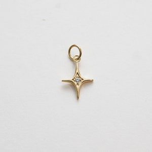 May include: A gold-toned star charm with a small clear rhinestone in the center. The charm has a loop at the top for attaching to a necklace or bracelet.