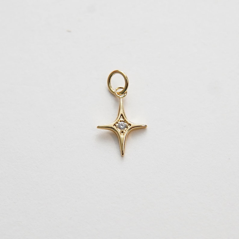 May include: A gold-toned star charm with a small clear rhinestone in the center. The charm has a loop at the top for attaching to a necklace or bracelet.