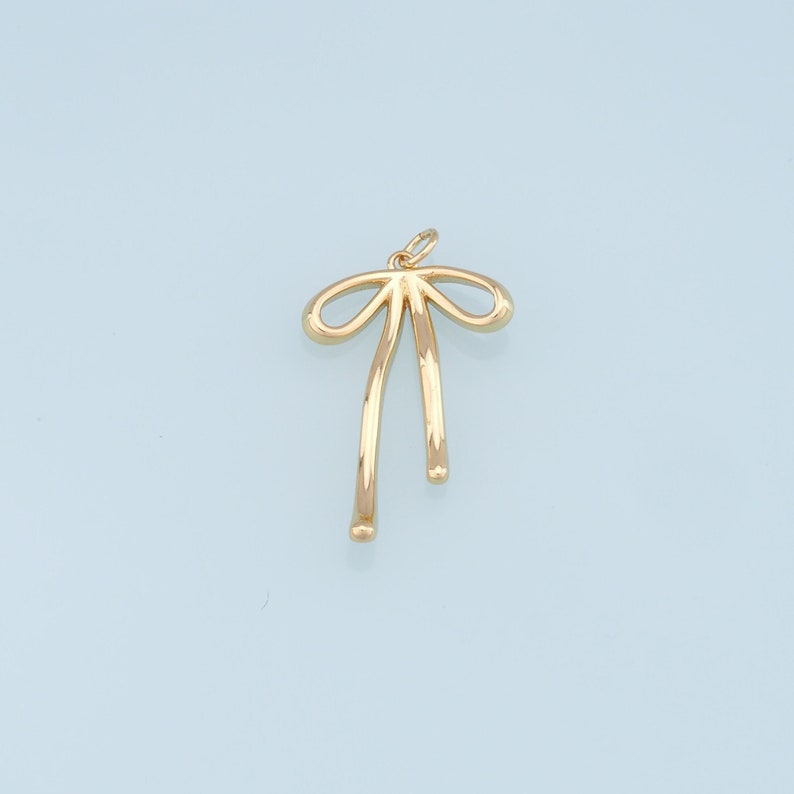 May include: A gold-colored bow charm pendant. The bow is tied with two long tails.