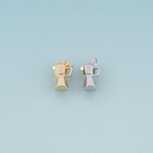 May include: Two small metal charms shaped like moka pot coffee makers. One charm is finished in a polished gold tone, and the other is finished in a polished silver tone. Each charm features a small loop at the top for attachment to jewelry.