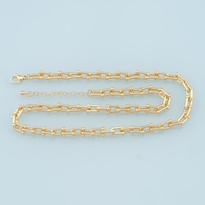 Könnte beinhalten: Eine goldene Kettenkette mit einem zarten, verlinkten Design. Die Kette besteht aus kleinen, runden Gliedern, die in einem sich wiederholenden Muster miteinander verbunden sind. Die Halskette ist etwa 46 cm lang und hat einen Karabinerverschluss.