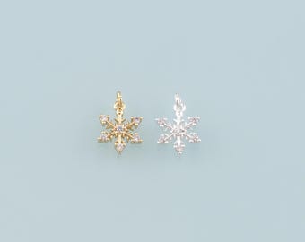 May include: Two snowflake charms, one gold-toned and one silver-toned, each adorned with small, clear crystals. The charms are set against a light blue background, ideal for jewelry making or holiday crafts.