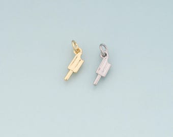 May include: Two small charms in the shape of ice lollies. One is gold-coloured, and the other is silver-coloured. Each charm has a small loop at the top for attaching to a necklace or bracelet. The charms are on a light blue background.