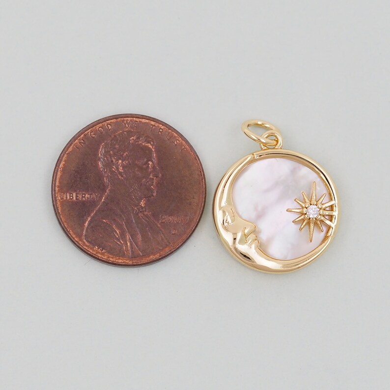 May include: Gold pendant charm featuring a crescent moon with a face and a star with a single clear rhinestone. The pendant is approximately the size of a US penny.