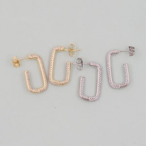 May include: Two pairs of earrings, one gold and one silver, with a square shape and a row of small clear stones around the edge.