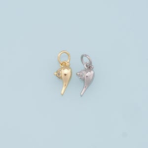 May include: Two gold and silver seashell charms with a small crystal on the top. The charms are on a light blue background.