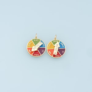 May include: Two gold-colored charms with a colorful wheel design. Each wheel has the words "this", "that", "me", "you", "it", and "off" printed on it. The wheels have a spinning arrow that points to the word "you" on both charms.