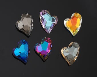 May include: Six heart-shaped crystal embellishments in various colours, including grey, blue, purple, and orange. Each crystal has a faceted design and a hole at the top for stringing or attaching. The crystals are displayed on a black background.