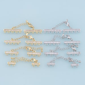May include: A set of 10 gold and silver extender chain connectors with clear crystal accents. Each connector has a bar with five loops and a chain with a lobster clasp.