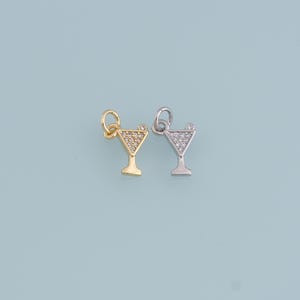 May include: Two cocktail-shaped charms, one gold-toned and one silver-toned, each with a loop for attachment. The martini glass shape is filled with small, clear stones. A small, clear stone is at the top of each charm.