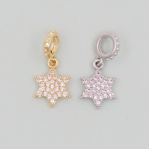 May include: Two gold and silver charm pendants in the shape of a six-pointed star with clear cubic zirconia stones.