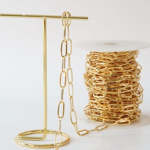 May include: A spool of gold-colored chain link, with a length of the chain draped over a gold metal stand.