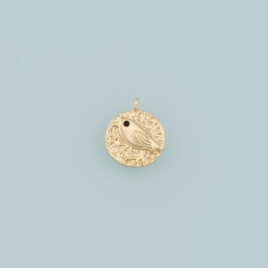 Peut inclure: Charme de pendentif en or avec un motif d'oiseau détaillé avec un œil noir. Le charme est rond et a une surface texturée.