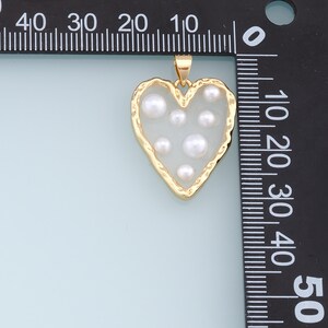 May include: A gold heart-shaped pendant with a white enamel background and six white pearl accents.