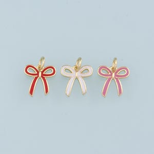 May include: Three gold-colored bow charms with enamel accents. The bows are red, white, and pink.