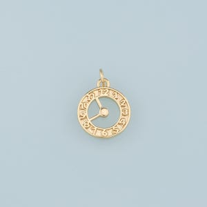 May include: Gold-toned clock charm with Roman numeral markings around the edge. The clock face is open and has a small circle in the center.