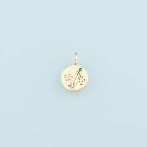 May include: Gold pendant charm with a round shape and a floral design. The flower is red and green.
