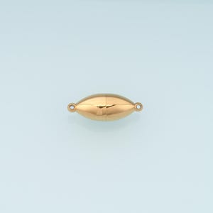 May include: A rose gold-toned magnetic jewelry clasp with a smooth, elongated oval shape. The clasp features a central seam where the two magnetic halves meet and includes a small circular loop on each end for attaching to jewelry chains or cords.