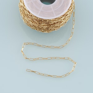 May include: A spool of gold-colored chain with a section of the chain unraveled. The chain is made of small, rectangular links.