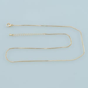 May include: A gold chain necklace with a lobster clasp closure. The chain is made of small, square links.