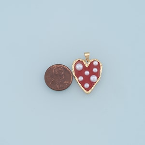May include: Gold heart-shaped pendant with a red enamel finish and white pearl accents.