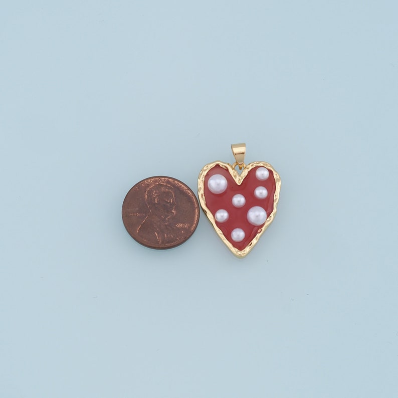 May include: Gold heart-shaped pendant with a red enamel finish and white pearl accents.