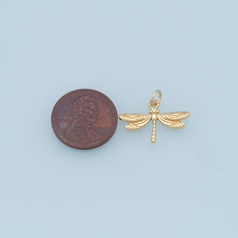 May include: Gold-toned dragonfly charm pendant, shown next to a US penny for size comparison.
