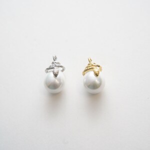 May include: Two pearl charms with a snake design. The charm on the left has a silver snake, and the charm on the right has a gold snake.