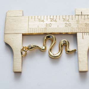 Op de afbeelding: Een gouden slangenbedel met drie kleine, heldere diamanten. De bedel wordt gemeten met een liniaal.