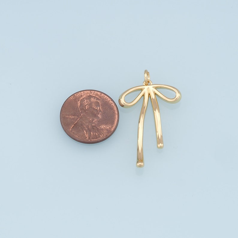 May include: Gold-toned metal bow charm pendant. The charm is about the size of a US penny.