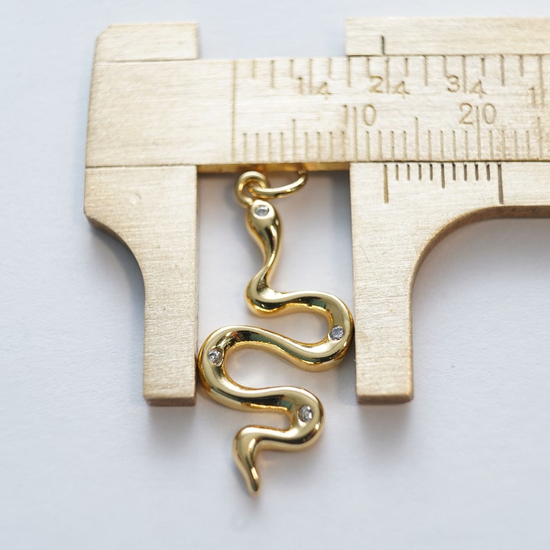 Op de afbeelding: Een gouden slangenbedel met heldere strasssteentjes, gemeten met een liniaal. De slang is ongeveer 6,5 cm lang.