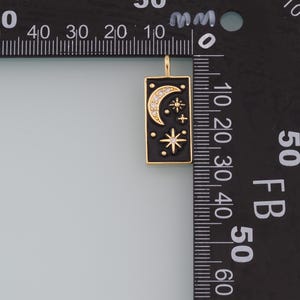 May include: A gold-toned pendant charm with a black enamel rectangle featuring a crescent moon and stars with clear rhinestones. The charm is approximately 2 cm in length.