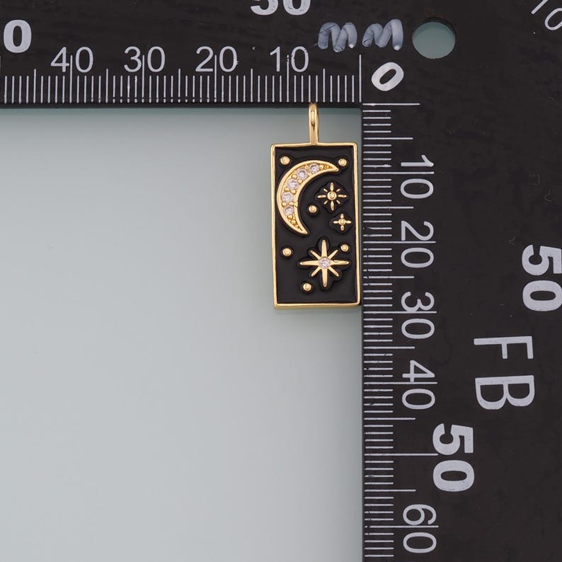 May include: A gold-toned pendant charm with a black enamel rectangle featuring a crescent moon and stars with clear rhinestones. The charm is approximately 2 cm in length.