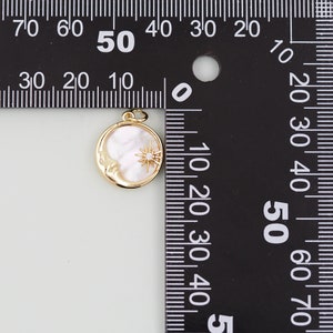 May include: A gold-tone pendant featuring a crescent moon with a face and a star with a clear rhinestone in the center. The moon is made of white mother-of-pearl. The pendant is approximately 1.5 inches in diameter.