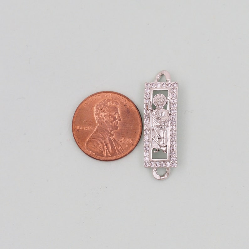 May include: Silver charm with a clear crystal border and a depiction of a saint inside. The charm is about the size of a UK penny.
