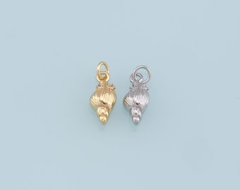 Op de afbeelding: Twee schelpbedels, een gouden en een zilveren, elk met een klein, helder strasssteentje. De bedels worden getoond tegen een lichtblauwe achtergrond.