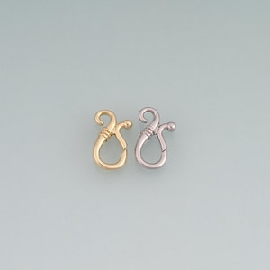 May include: Two jewellery clasps, one in a polished gold tone and one in a polished silver tone. Each clasp features a curved, hook-like design with a small ball end and a textured, wrapped detail at the neck, forming a secure loop for jewellery.