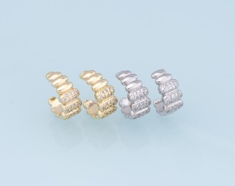 Pode incluir: Três pares de brincos de orelha, um dourado, um prateado e um de ouro rosa, cada um com uma fila de pequenas pedras de zircônia cúbica transparentes.