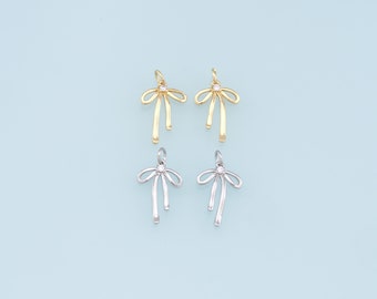 May include: Two pairs of bow-shaped charms with a small clear rhinestone in the center. One pair is gold and the other is silver.