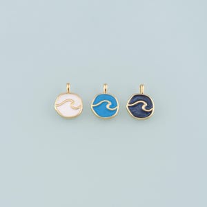 May include: Three gold-coloured pendants with wave designs. Each pendant features a circular shape with a gold border and a wave design in white, blue, and navy blue. The pendants are displayed on a light blue background.
