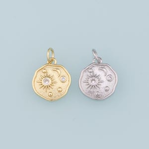 May include: Two gold and silver charms with a sun, moon, and stars design. The charms are round and have a textured surface.