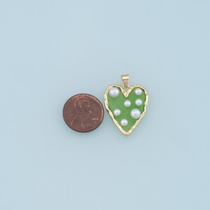 May include: A gold heart-shaped pendant with a green enamel finish and white pearl accents.