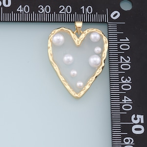 May include: A gold heart-shaped pendant with a white background and several white pearl accents.