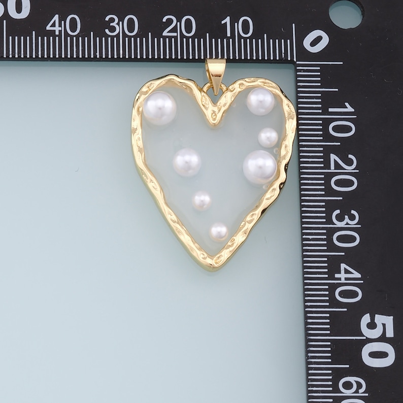 May include: A gold heart-shaped pendant with a white background and several white pearl accents.