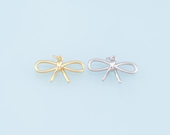 May include: Two gold and silver bow charms. The charms are in the shape of a bow with a knot in the center. The charms are on a light blue background.