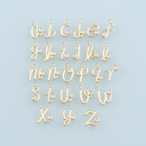 Puede incluir: Un conjunto de 26 abalorios de alfabeto de tono dorado con un solo strass transparente en cada abalorio. Los abalorios están en una fuente cursiva.