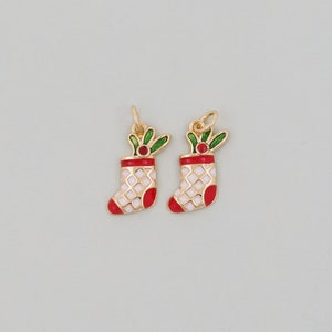 May include: Two gold-tone Christmas stocking charms with white and red enamel details and green holly accents.
