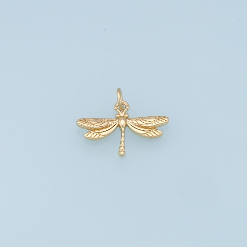 May include: A gold-colored dragonfly charm pendant. The dragonfly has detailed wings and a body with a small loop at the top for attaching to a chain or bracelet.